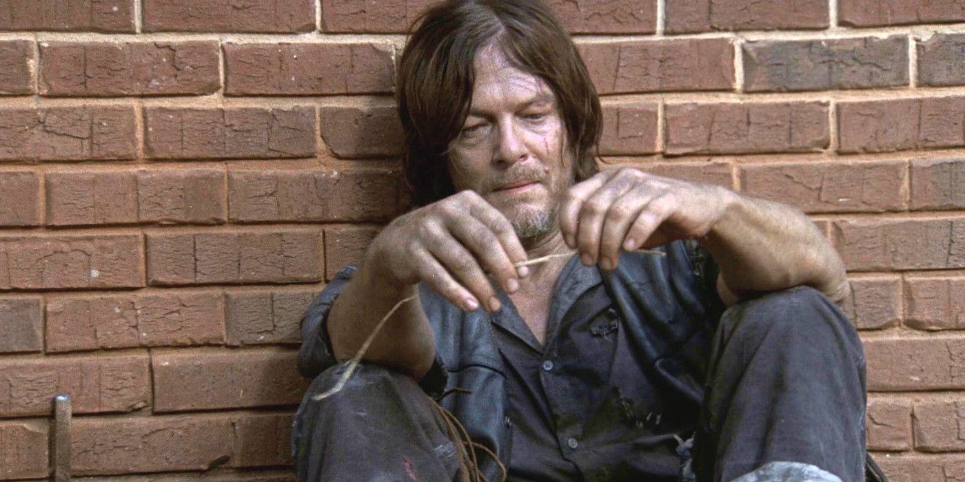 Norman Reedus as Daryl In The Walking Dead all covered in grime sitting against a brick wall looking sad